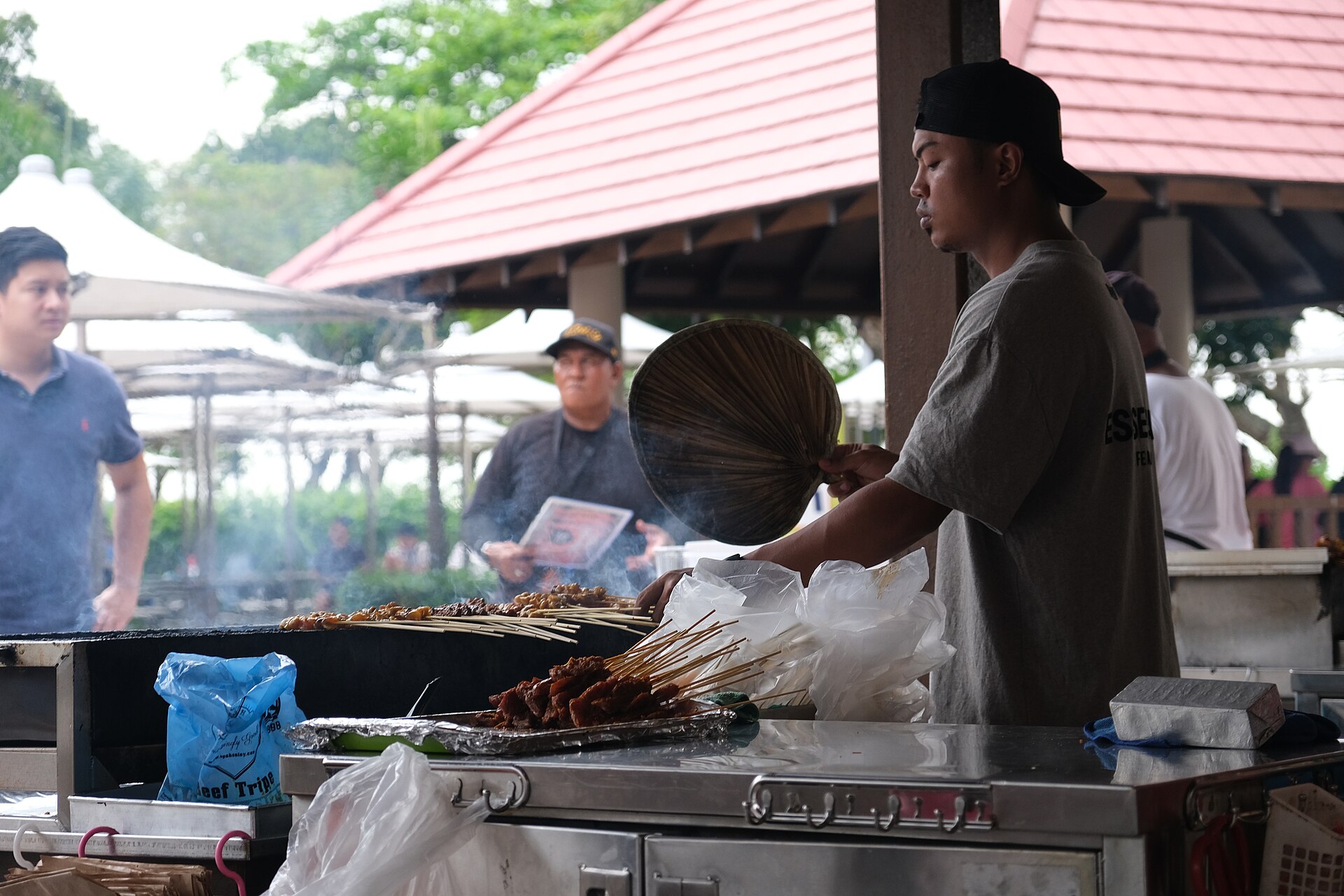 Satay skewers grilling over charcoal at a stall in East Coast Lagoon Food Village, fanned by hand